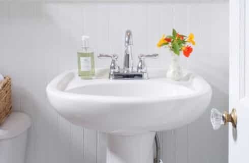 White pedestal sink with yellow and orange flowers in a vase and bottle of hand-soap.